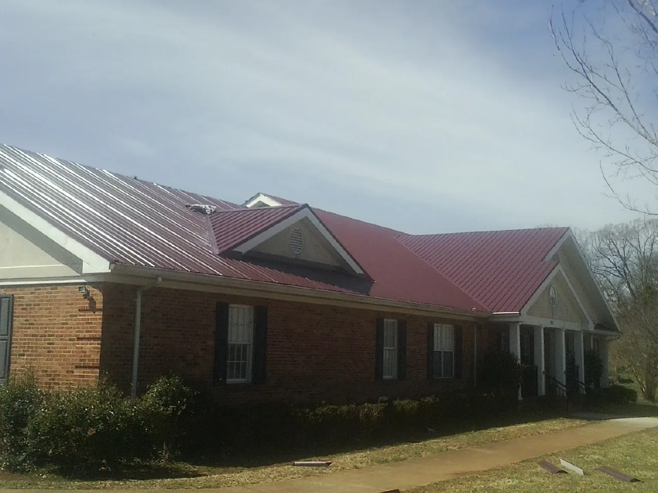 Red metal roof with gabled entries on a long brick building, from a Hail Damage Roof Repair job in Checotah