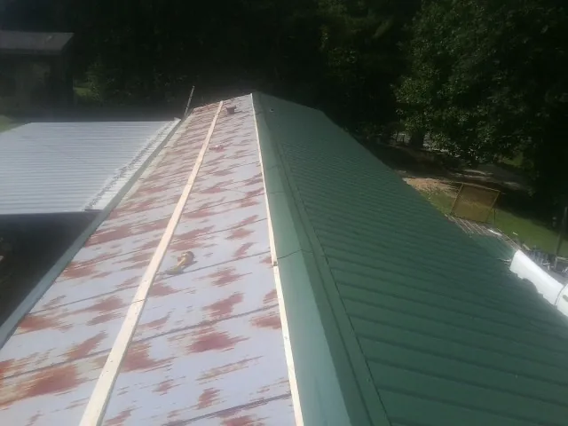 Old rusted panels beside newly installed green metal roofing — Wind Damage Roof Repair by Roofing Brothers in Checotah