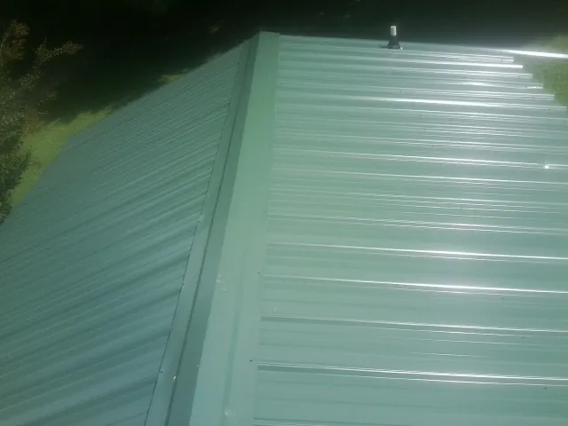 New green metal panels meeting at the ridge of a roof — Flat Roof Repair work by our crew in Checotah