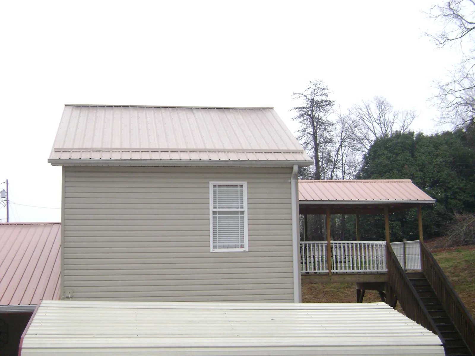 Tan metal roofs on a two story addition and attached porch, from a Roof Replacement job in Checotah